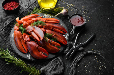 Boiled red lobster claws with spices and parsley on a black stone plate. On a black background. Rustic style. Seafood delicacies.