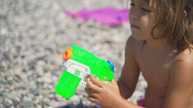 A child plays with a water gun in the summer at sea. Cute little girl holding a water gun on the beach by the sea