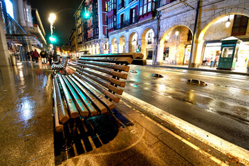 Wooden bench wet at nightfall with rain in front of the Ribera arcades in Bilbao