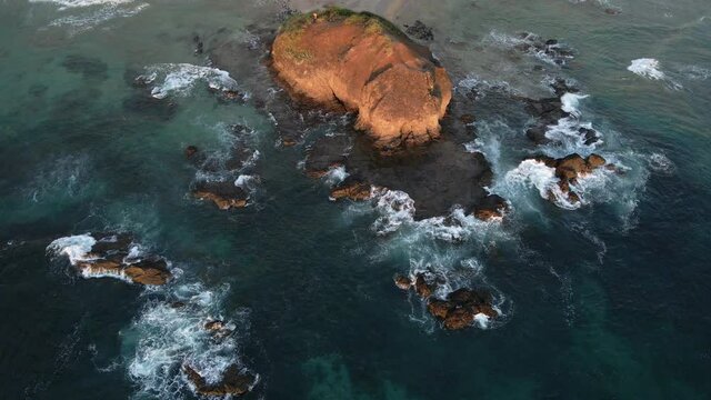 Multiple large rocks in the shallow water of the south pacific ocean. South American beach during sunset with warm tones captured by 4k drone.