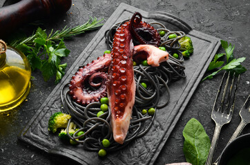 Black pasta with octopus tentacles on a black stone plate. Seafood. Top view. Free space for your text. © Yaruniv-Studio