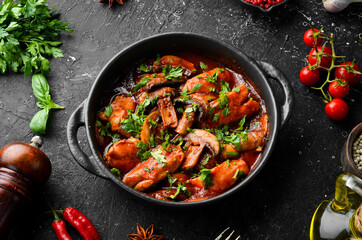 Baked mushrooms with chicken fillet in tomato sauce. In a black stone plate. Top view.