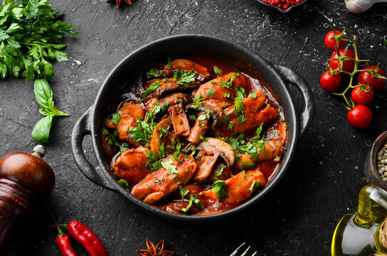 Baked mushrooms with chicken fillet in tomato sauce. In a black stone plate. Top view.