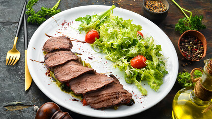 Baked veal steak with salad and vegetables. On a black background. Top view. Rustic style.