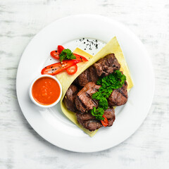 Juicy kebab with pita bread and sauce on a white plate. Top view.