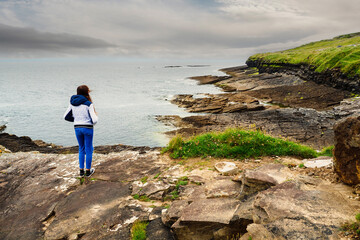 Teenager girl looking at the ocean and beautiful coast line. Mullaghmore, county Sligo, Ireland. Travel and holiday concept. Cloudy sky. Irish landscape.