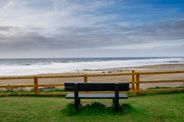 Fototapeta na wymiar Empty wooden bench with view on amazing Fanore beach, county Clare, Ireland. Beautiful cloudy sky over ocean. Irish landscape. Popular tourist destination.