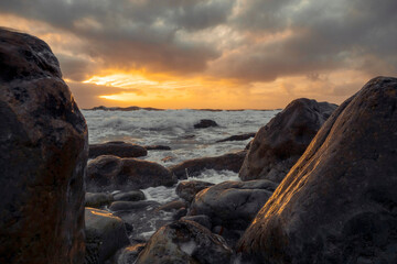 Ocean at sunset. Warm light reflection on rough rocks. Ocean waves rushing towards the coast....