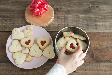 Heart-shaped cookies with filling. Woman's hand filling cookie box.