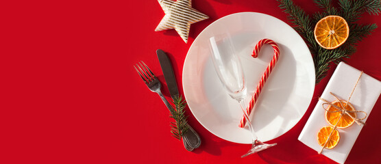 Christmas served dinner, table design on red background. White plate, champagne glass, gift present...