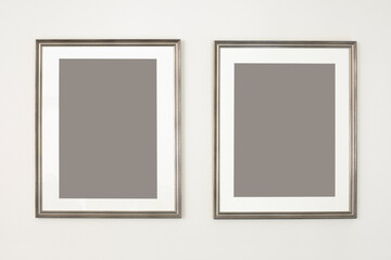 Two vertical frames, poster mock up. Empty silver picture frames hanging on the wall. Free space for your picture or text, copy space. Minimalist design.
