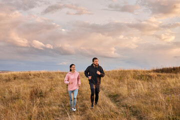Young couple athlete runners breathing fresh air in morning. Healthy man and woman doing fitness jogging on field. Training run. Free people runs in summer at dawn. fit couple in sports clothes