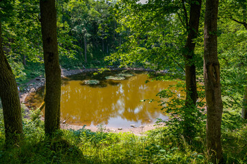 Round lake in Kaali meteorite crater. Estonian island of Saaremaa. Green steep slope and trees...