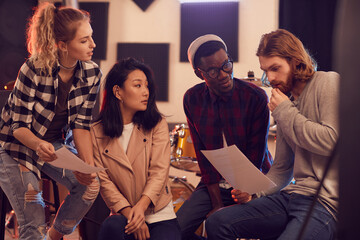 Multi-ethnic group of young people writing music together while rehearsing in record studio