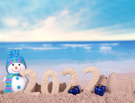 2022 and sand castles with snowman and gifts on beach in sand