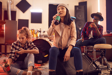 Multi-ethnic group of young people in music studio focus on Asian young woman drinking beet in...