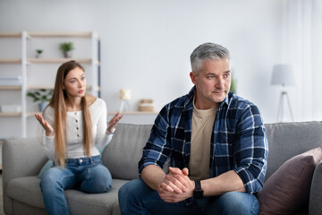 Mature married couple having fight, angry woman arguing with unhappy man in living room, copy space
