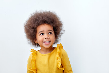 Close up portrait of little adorable African american child girl looking at side, having fun isolated over white studio background. Copy space for advertisement. Human emotions, children concept