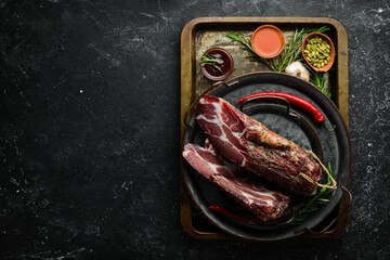 Dried and salted piece of meat. Prosciutto, jamon, on a black stone background. Top view. Free...