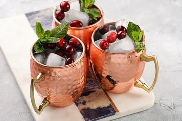 Türaufkleber Traditional american alcoholic beverage moscow mule in copper mugs with cranberry and mint on white marble board - non-alcoholic cocktail version © Romana