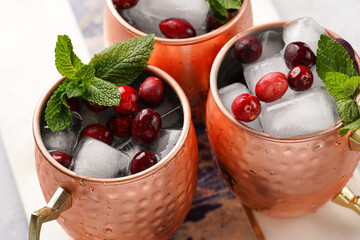 Traditional american alcoholic beverage moscow mule in copper mugs with cranberry and mint on white marble board - non-alcoholic cocktail version
