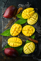 Obraz na płótnie Canvas Fresh tasty sweet mango with leaves on old wooden dark background. Rustic style. Top view. Tropical fruits.