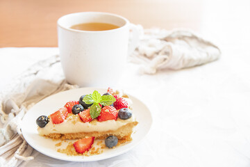 piece of strawberry and blueberry cheescake on plate and cup of tea served for breakfast at home, hotel or cafe. Dessert meal, sweet food . High quality photo