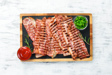 Fried pieces of bacon on a black stone board. Top view. Free space for text.
