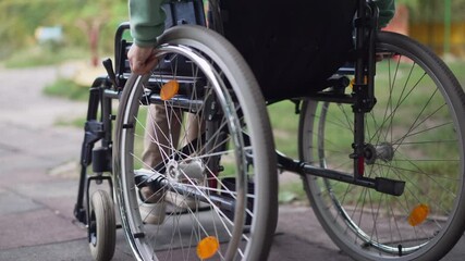 Tracking shot child rolling manual wheelchair outdoors. Unrecognizable Caucasian boy riding assistive device in summer park. Disability and childhood lifestyle