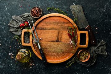 Wooden tray with utensils, spices and vegetables on a black stone background. Restaurant menu....