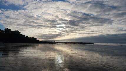 Plage du Minihic à Saint-Malo en Bretagne, paysage de côte avec le reflet d'un ciel nuageux sur le sable mouillé, au bord de la mer (France)