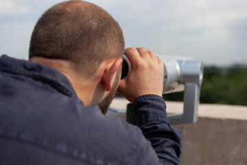 Closeup of caucasian male looking through binoculars touristic telescope. View from the observation point standing on tower rooftop. Tourist enjoying metropolitan city landscape during vacation