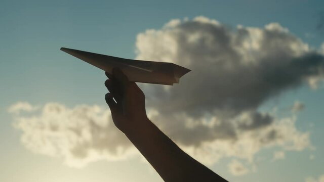 Mano con aereo di carta e sfondo nuvole, 
