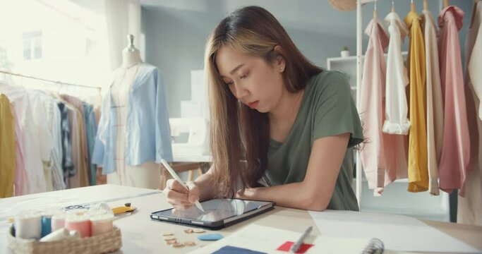 Professional Asia female fashion designer with casual use digital tablet create new collection in her shop creative office. Lady tailor study draw sketch on tablet site at work in university studio.