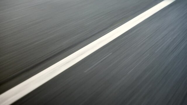 Tarmac road surface slow motion showing motion blur with white lines passing under the car. Gtreat B roll for automotive subject or to show speed or travel.
