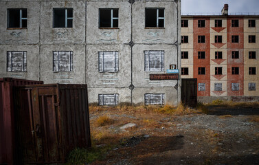 Abandoned panel buildings in the Arctic. Some of the windows are covered with boards. Rusty containers near houses. Signboards with the name of Ryntyrgina street. Egvekinot, Chukotka, Far East Russia.