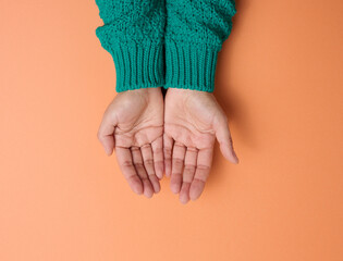 two female hands folded palm to palm on a orange background, top view