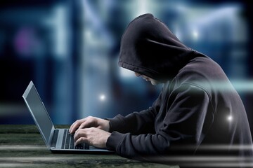 A hacker in hood working at computer typing text in dark room,