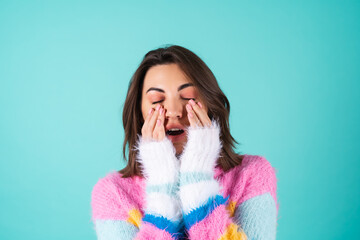 Young woman in a bright multicolored sweater on a blue background sleepy eyes, cute yawns, lack of sleep