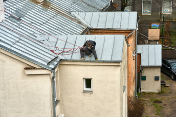 A man tied with a red rope for safety cleaning a drain pipe on the roof of a house.
