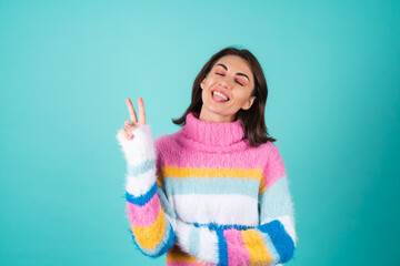 Young woman in a bright multicolored sweater on a blue background cute smiling, playful, showing...