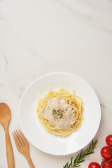 pasta concept a dish of boiled long slim pasta being served on the white tile table together with a wooden spoon and fork, tiny red tomato, and other ingredients