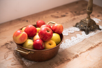 Some fresh eco read apples on a cooper basket placed on a wooden table. Decor with bio food products.