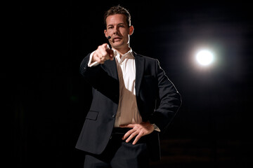 speaker with microphone pointing finger to the listener, standing on stage with projector in...