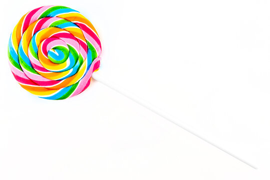 Sweet colorful spiral shaped lollipop lying in upper left corner, isolated on white background, top view.