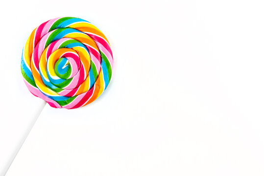 Sweet colorful spiral shaped lollipop lying in upper left corner, isolated on white background, top view.