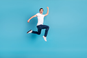 Fototapeta na wymiar Full size photo of young cheerful guy go run jump up hurry fast isolated over blue color background