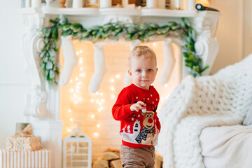 cute little boy in red Christmas sweater near fireplace with socks for gifts