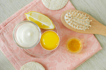 Raw egg yolk, greek yogurt (sour cream or kefir), lemon and wooden hairbrush for preparing diy face and hair masks, scrubs and moisturizers. Homemade beauty treatments recipe. Top view, copy space