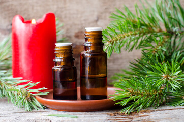 Small glass bottles with essential pine oil, pine branches and red burning candle. Aromatherapy, sauna, homemade spa and herbal medicine ingredients. Copy space.